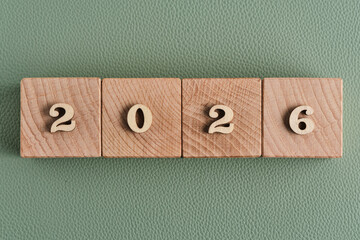 Wooden blocks forming year 2026 arranged in row on green leather textured background, minimal new year concept.
