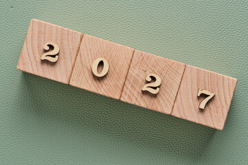 Wooden blocks forming year 2027 arranged in row on green leather textured background, minimal new year concept.
