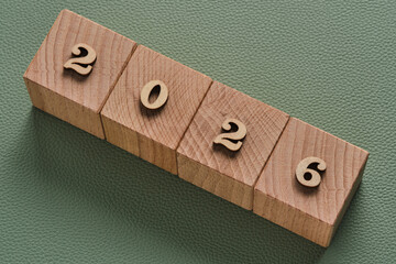 Wooden blocks forming year 2026 arranged in row on green leather textured background, minimal new year concept.