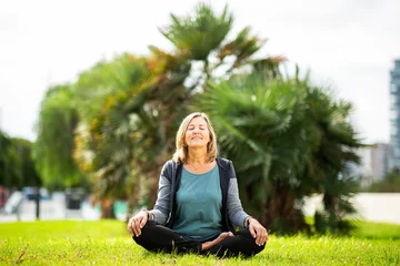 Fotobehang Lotusbloem Peaceful woman meditating in lotus pose on green grass  © Paula