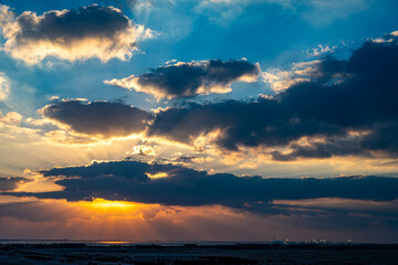 Obraz premium Dramatic Sunset Sky with Sun Rays and Clouds Over Coastal Horizon