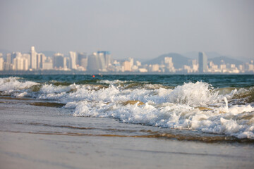 Sea sandy beach with surf waves on city buildings background. Background for travel and vacation