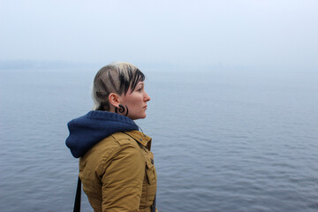 Natural, unretouched portrait of a young woman with an original shaved hairstyle and earring, standing by the sea. Authentic lifestyle image representing individuality, real beauty.  © Светлана Мищенко