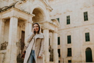 Fototapeta premium Woman walking in Malta while talking on the phone near historic architecture