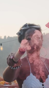 Vertical portrait shot of young African American woman dancing with smoke bomb on pier during lakeside party