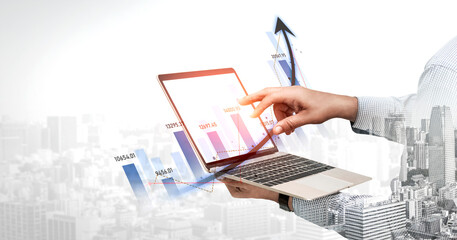 Obraz premium A business professional engages with financial data on a laptop, showcasing a growing trend in a digital format against an urban skyline background. Scalp