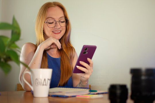mulher jovem branca e ruiva, mexendo no celular e sorrindo, redes sociais
