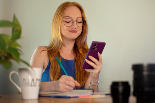 mulher mexendo no celular e fazendo anota&ccedil;&otilde;es no papel, uso de redes sociais de pessoas jovens