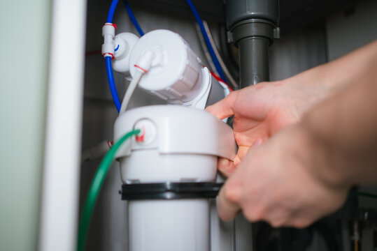 Hands installing new filter cartridge in an under sink reverse osmosis drinking water purification system, performing routine maintenance for clean, healthy water at home