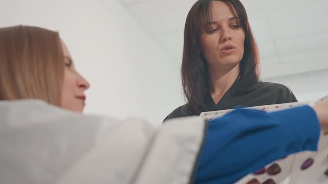 Salon consultation with color swatch board, female stylist and client examining hair dye samples, pointing at shades, comparing tones under bright studio lighting, calm professional atmosphere,