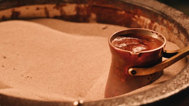 Making Traditional Turkish coffee on the sand, barista authentic Turkish coffee on hot sand in a copper coffee pot.