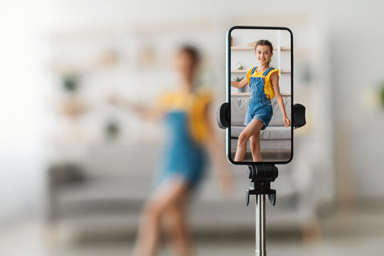 Modern Lifestyle Activity. Smiling female teenager influencer shooting trendy dance video for social media, selective focus on mobile phone screen on tripod stabilizer, closeup, blurred background