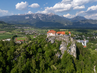 Aerial view of Bled Castle overlooking Lake Bled, Slovenia. Medieval fortress on a cliff captured by drone, surrounded by alpine landscape and clear blue water. Famous European travel destination and 