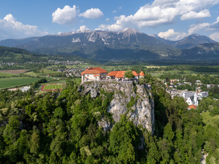 Aerial view of Bled Castle overlooking Lake Bled, Slovenia. Medieval fortress on a cliff captured by drone, surrounded by alpine landscape and clear blue water. Famous European travel destination and 