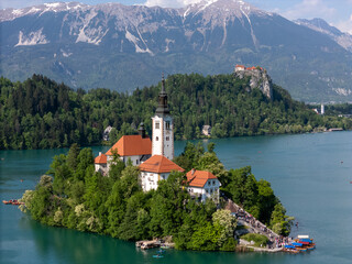 Aerial drone view of Bled Island with the Church of the Assumption in the middle of Lake Bled, Slovenia. The iconic island church is surrounded by turquoise alpine waters and forested mountains. Famou