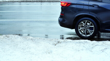 Fragment of black unidentifiable suv car, light alloy wheel with winter tires on road