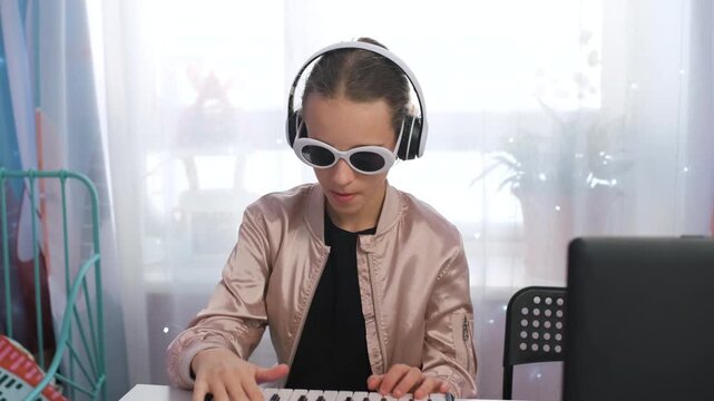 Girl wears headphones and sunglasses while making music on a midi keyboard, showing a fun and creative hobby during her time at home