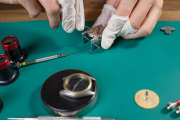 Professional watchmaker works on assembling a mechanical watch movement using precision tools on a clean workbench in a workshop.