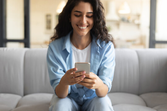 Pretty brunette woman using smartphone on couch, checking email, having video call with friend online at home, selective focus. Caucasian lady posting in social media, writing sms indoors - Powered by Adobe