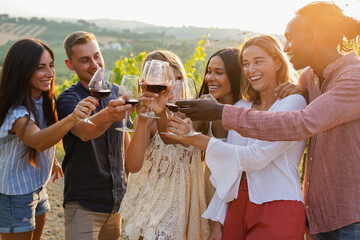 Obraz premium Group of happy friends cheering with red vine inside wineyards during sunset time - Multiracial people, party and wine tasting concept