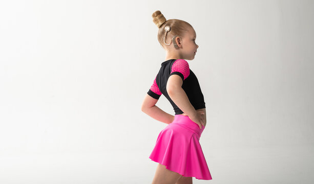 Smiling dancer with cochlear implant posing in pink costume in studio. Copy space. Pediatric hearing support, inclusive sport and childhood confidence through expressive dance movement