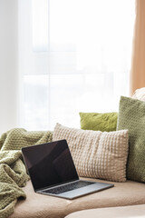 Laptop on Cozy Sofa with Textured Pillows and Blanket. Relaxed Home Workspace