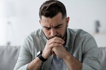 Man sit on sofa and feeling stressed at bad news, depression, loneliness. Sad attractive bearded...
