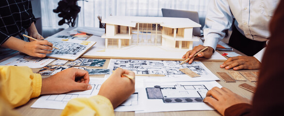 A group of architects collaborates in a bright workspace, reviewing blueprints, sketches, and a scale model, showcasing teamwork and creativity in building design. SACTR