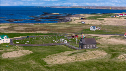 Fototapeta premium Aerial drone view of Hvalsneskirkja church on the Reykjanes Peninsula in Iceland. The historic stone church stands near the rugged Atlantic coastline, surrounded by lava fields and dramatic Nordic lan