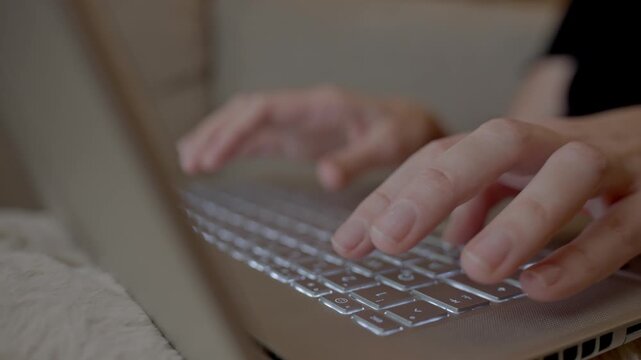 Hands typing on laptop keyboard while sitting on sofa at home. Concept of remote work and online communication