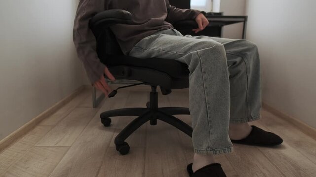 Man adjusting office chair height in modern home office workspace with computer desk, ergonomic furniture setup for comfortable remote work and productivity indoors
