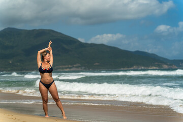A beautiful girl poses on the beach against the backdrop of sea waves