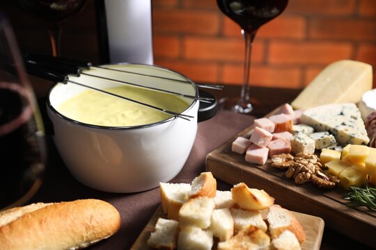 Fondue pot (caquelon) with melted cheese, wine and snacks on table, closeup