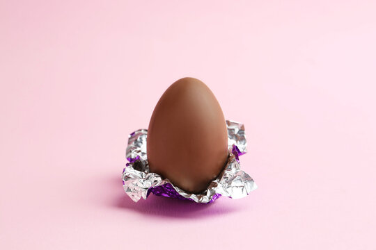 Chocolate egg with foil on pink background. Happy Easter