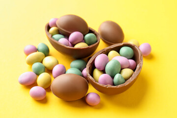 Obraz premium Tasty chocolate eggs with colorful candies on yellow background, closeup. Happy Easter