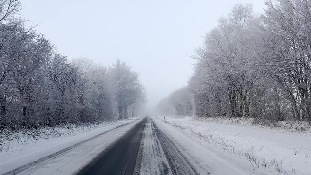 View from a car driving on icy road in winter at countryside in Europe, trees covered with snow 