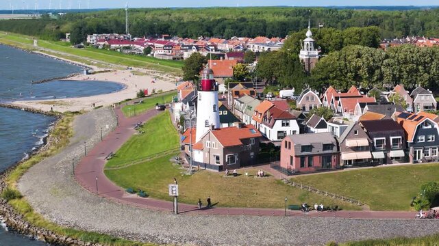 distinctive white lighthouse stands edge neighborhood bordered by stone seawall elevated perspective wind turbines horizon urk netherlands flevoland coastal defense landmark renewable energy 