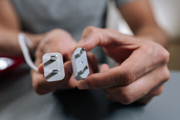 Male hands holding electrical plug with uk type g connector and european type c travel adapter, illustrating power compatibility for charging devices while traveling internationally.