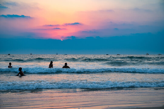 Sunset at Colva Goa beach in South India, silhouette of people swimming in Arabian Sea, tropical west coast, Asia, vacation destination