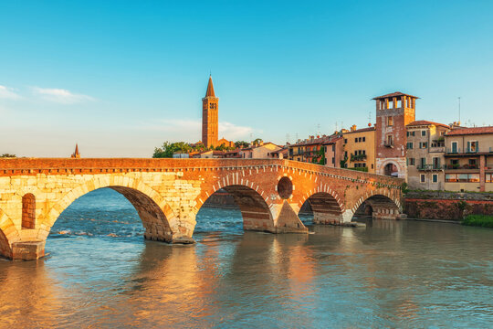 Historic stone Ponte Pietra bridge in Verona old town crossing Adige River with historic buildings and church tower at sunrise, Veneto, Italy. Skyline of Italian city. Travel destination in Europe