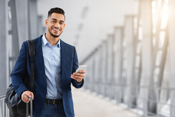 Portrait Of Young Middle Eastern Man With Smartphone In Hand Waiting At Airport, Happy Smiling Arab...