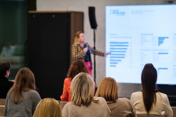 Presenter explains charts to listeners during seminar audience focus on data and insights shown on big screen graphs and statistics.