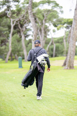 A man is walking on a golf course with his golf bag
