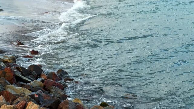Waves crashing on rocks at the shore during daylight hours in a coastal area. Waves move in and out, hitting the rocks at the edge of the water.