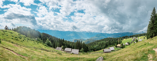 Planina Zajamniki features a village nestled in the hills with houses scattered among trees. Clouds gather above the mountains in the distance.