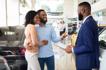 Obraz premium Family Buying Car. African American Spouses Purchasing New Vehicle In Dealership Center, Happy Black Couple Discussing Contract Details With Smiling Salesman In Modern Showroom, Closeup Shot