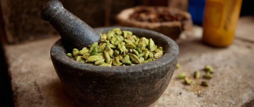 A rustic mortar and pestle filled with cardamom pods.