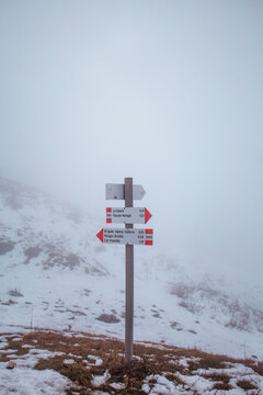 Cartello con informazioni sui sentieri di montagna in Italia, circondato dalla neve e dalla foschia.