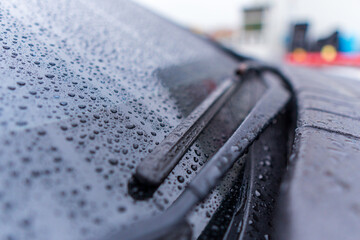 Rain accumulates on a car windshield with wipers ready for use during a cloudy day in the city