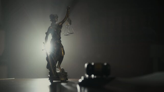 POV Statue of Justice figurine standing on a desk in a dark law office with soft dramatic lighting. law, fairness, legal system, justice environment. Move camera